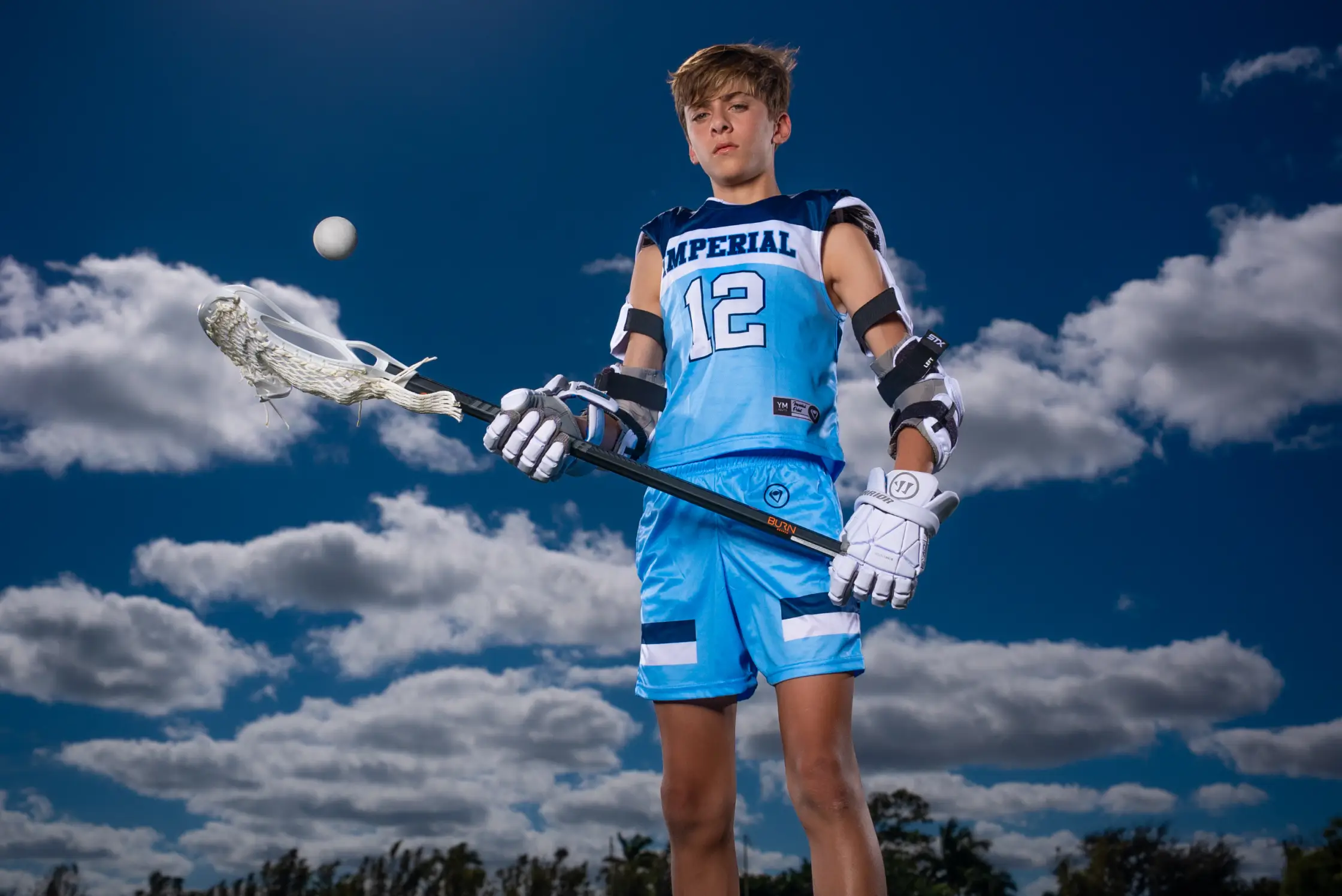 youth-lacrosse-jerseys Youth lacrosse player holding a lacrosse stick, tossing a ball in the air.