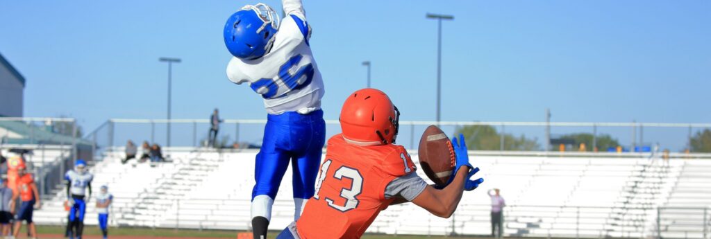 High school football players in action, wearing sublimated jerseys on a sunny day.
