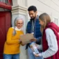 Two volunteers fundraising outside a home as a smiling woman signs a clipboard on her doorstep.