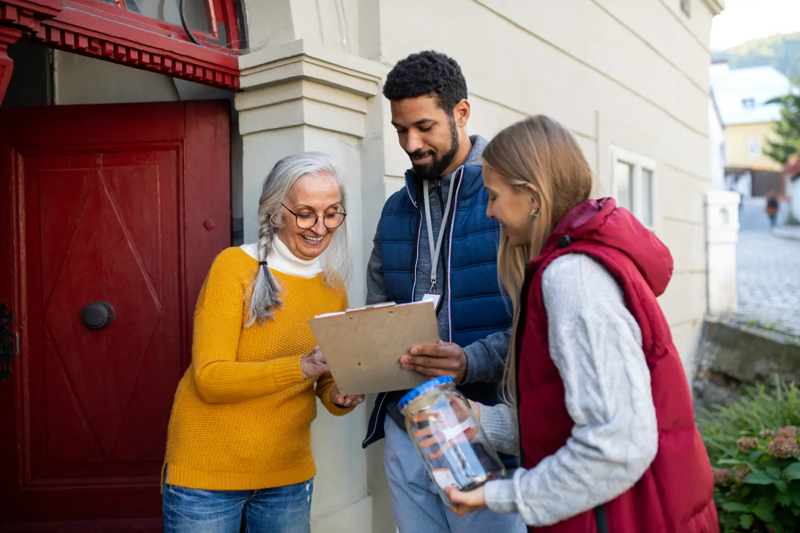 Two volunteers fundraising outside a home as a smiling woman signs a clipboard on her doorstep.