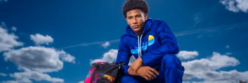 athlete wearing a custom sublimated blue Imperial Point warm up jacket seated with a team duffle bag
