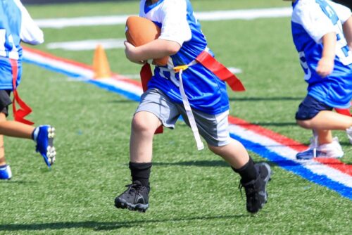 Youth players wearing custom 7 on 7 flag football jerseys running on a turf field.