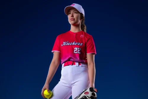 Softball player wearing a custom sublimated red Huskers jersey with number 22 and gradient design, paired with white pants and cap 